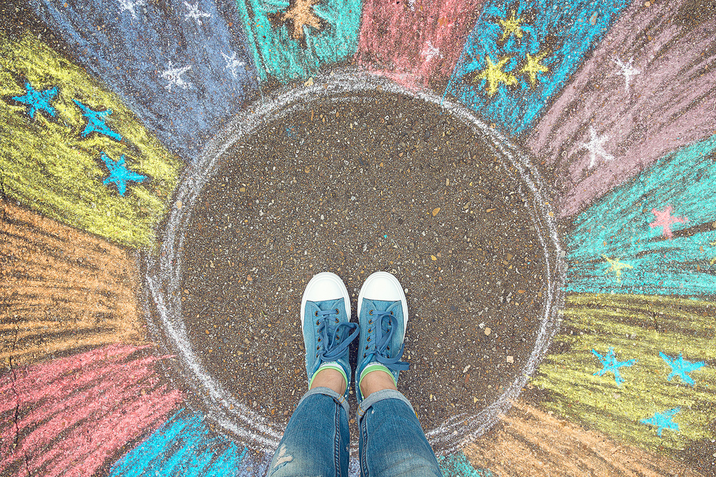 An illustrative photo of the comfort zone. Feet standing in an unmarked piece of street, surrounded by splashing colors and stars, illustrating the magic of stepping out of your comfort zone.