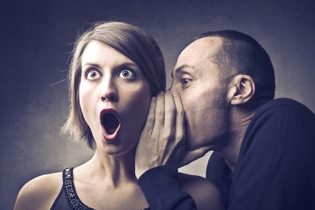 a man whispers a shocking secret into a woman's ear. sepia effect.